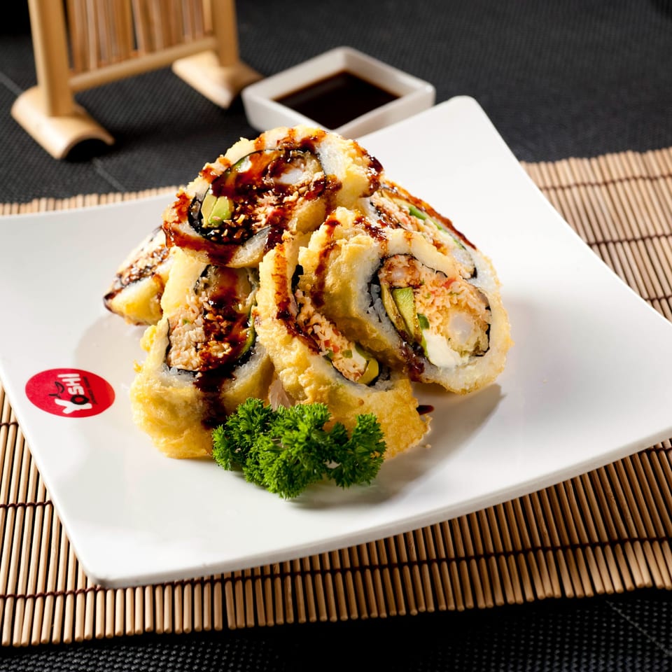 Tempura-fried sushi rolls with avocado, shrimp, and sauce, garnished with parsley on a white plate.