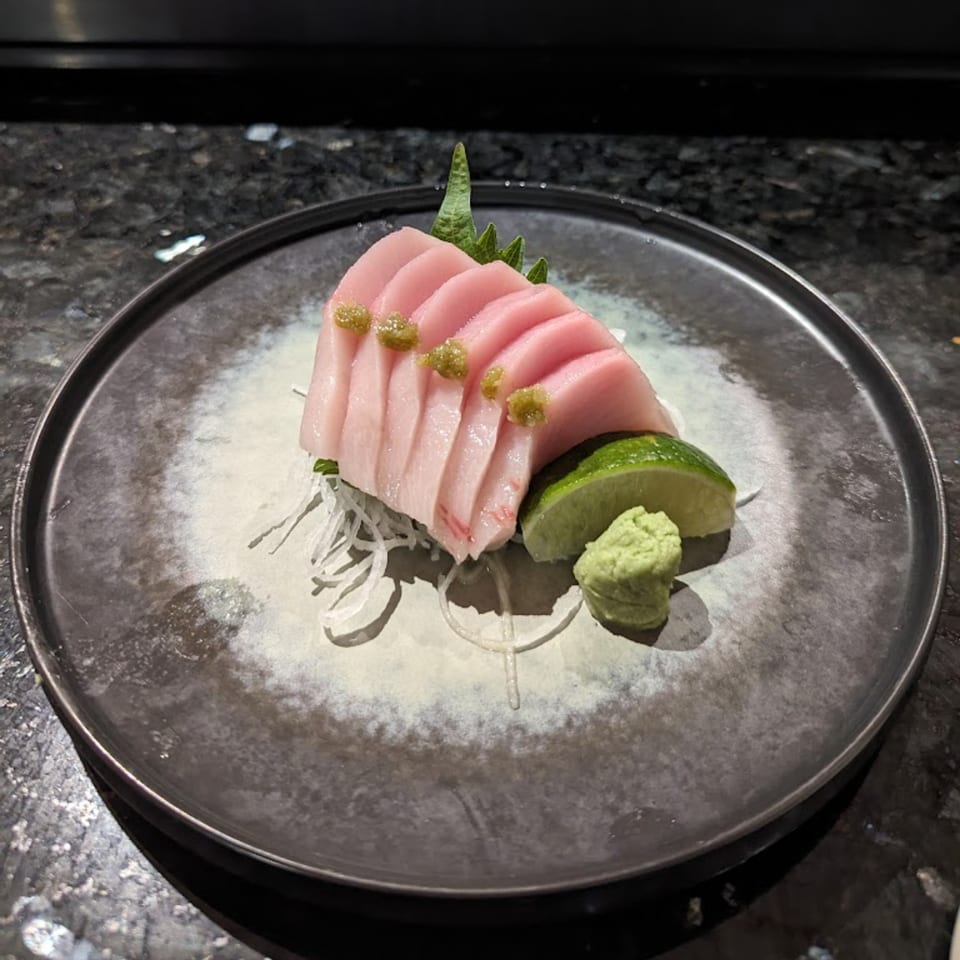 Fuji Japanese Cuisine's tuna sashimi with wasabi, lime, and shredded daikon on a dark plate.