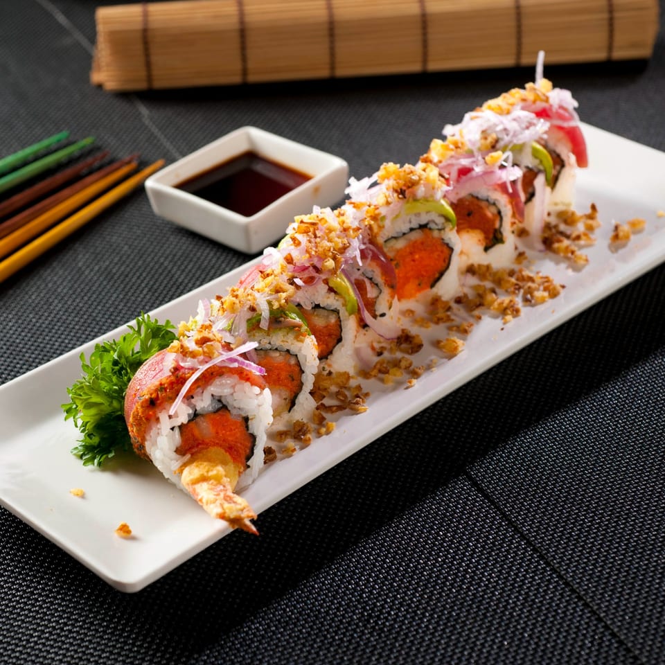 A long white plate of Fuji Japanese Cuisine sushi rolls with shrimp tempura, avocado, and crispy toppings.