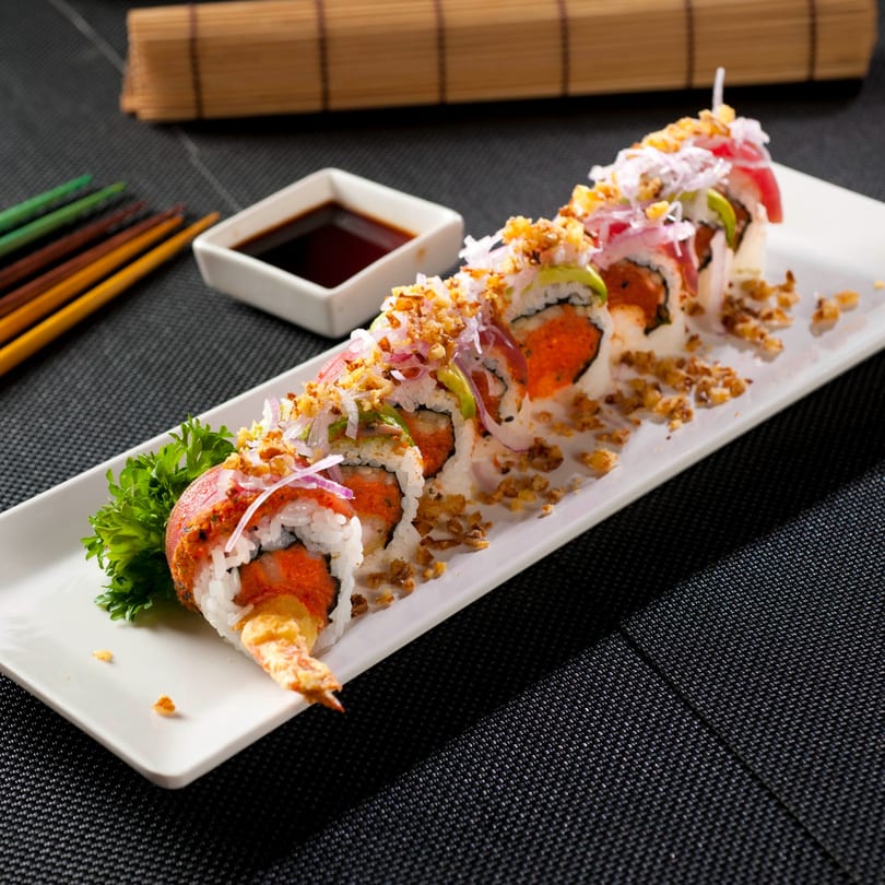 A long white plate of Fuji Japanese Cuisine sushi rolls with shrimp tempura, avocado, and crispy toppings.